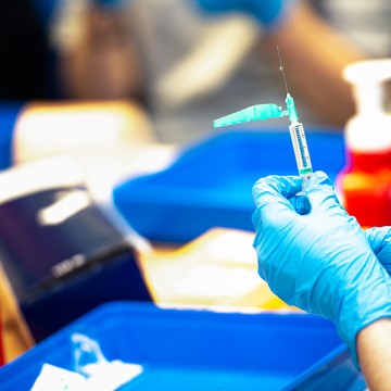 hand wearing a blue medical glove holding a syringe